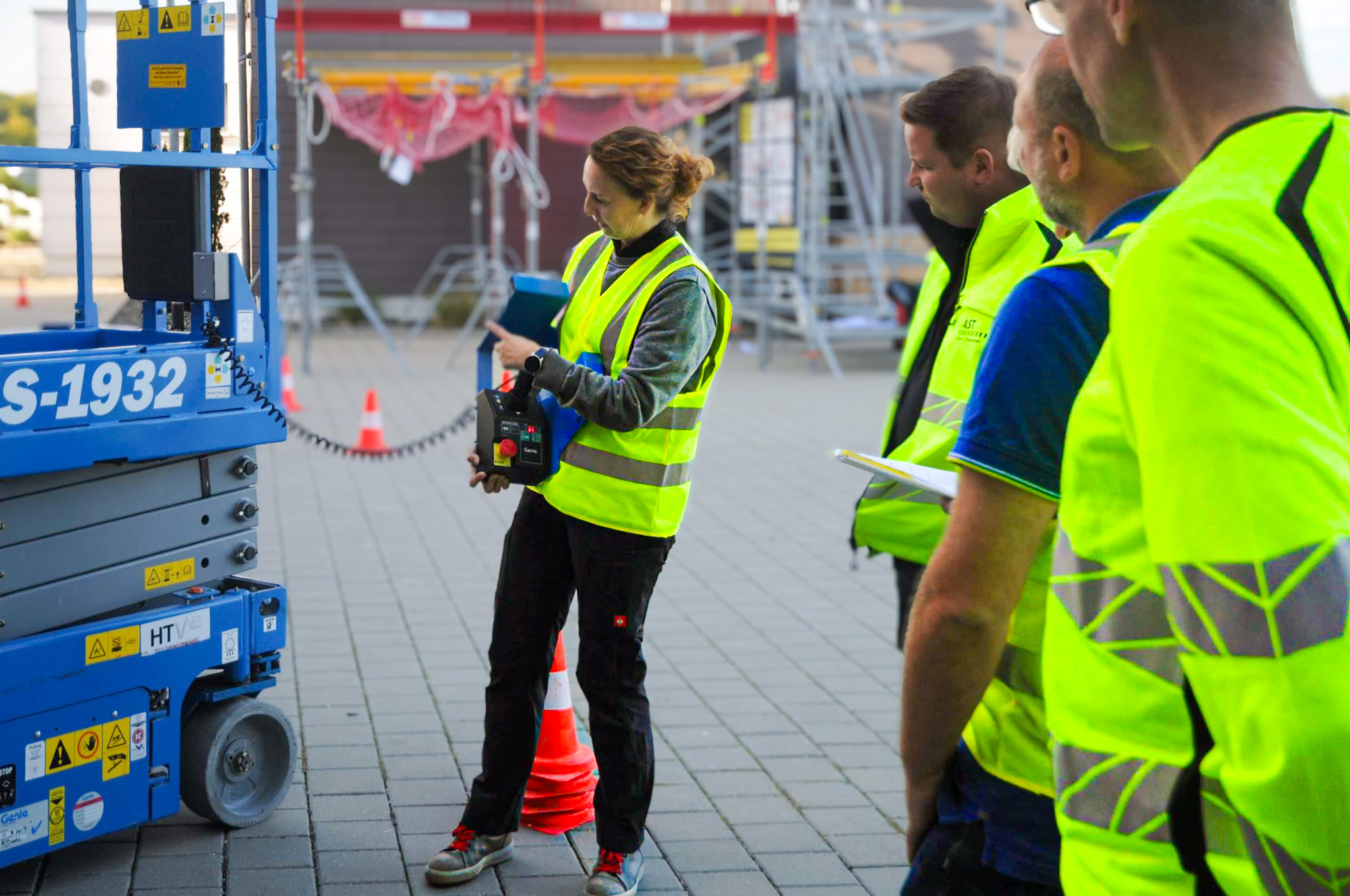 Ausbilderin erklärt einer Gruppe die Bedienung einer Hubarbeitsbühne am Bodensteuerpult.